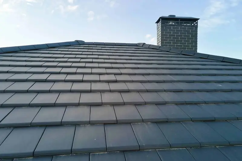 Newly laid dark grey roof tiles with a matching brick chimney against a blue sky