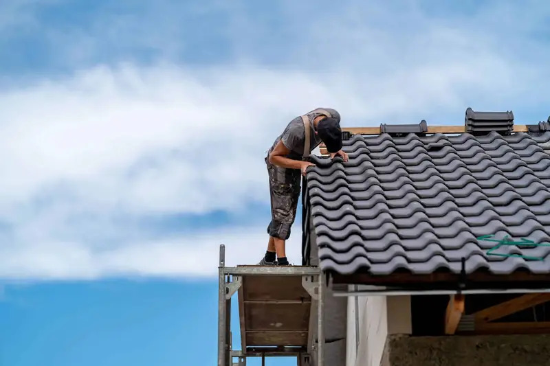 Roofer standing on scaffolding while laying grey interlocking tiles on a new roof