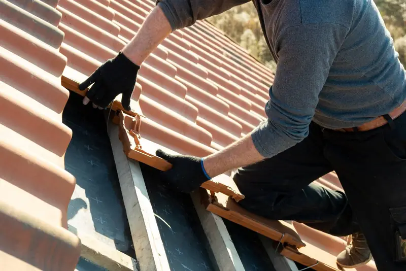Roofer lifting a broken clay tile out of a pitched roof during a repair