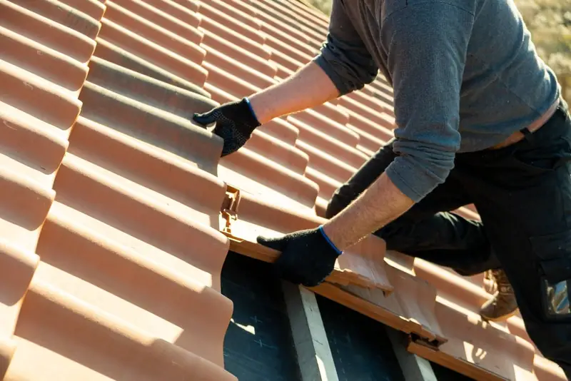 Roofer in work gloves fitting a terracotta interlocking tile on a pitched roof