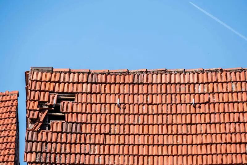 Clay tiled roof with a patch of missing and broken tiles after storm damage
